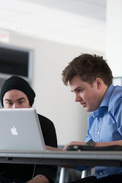 two students sitting beside each other looking at the same Apple laptop screen.