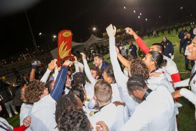 Humber Hawks soccer players celebrate as one holds up a championship trophy.