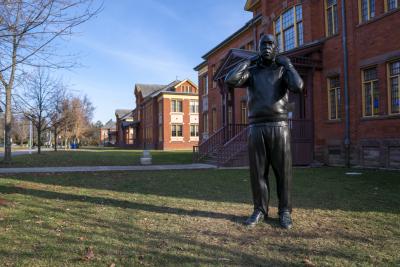 Cover Up (The Reveal), Thomas Price's 9-ft bronze statue of a Black male walking, pulling his hood up, stands outside C Cottage