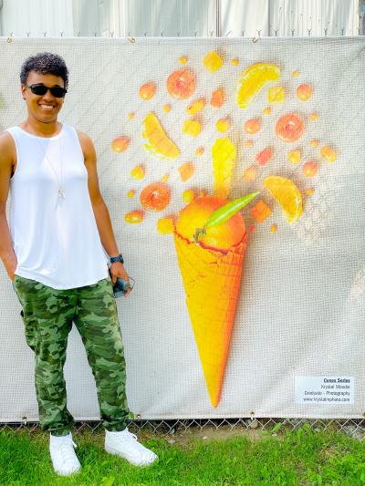 Krystal Moodie stands in front of one of her Cones pieces - a yellow waffle cone filled with yellow fruits and candies