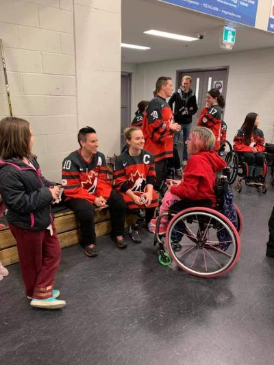 Claire Buchanan sits in a hockey locker room, speaking with with other young, female para athletes