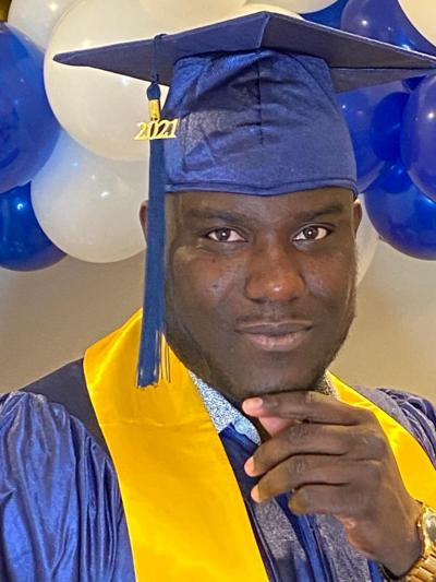 Avion Campbell smiles slightly at the camera wearing a blue cap and gown with a yellow convocation collar.