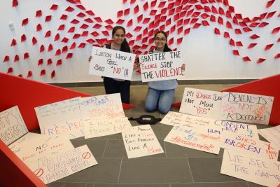 Two people hold up signs that read ‘Listen when a girl says no’ and ‘Shatter the silence. Stop the violence.’