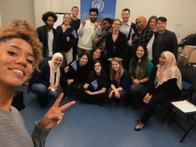 Larissa smiles in the foreground of a selfie, making the peace sign. A group of young people behind her smile at the camera.