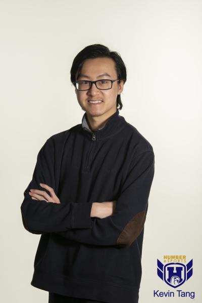 Kevin Tang crosses his arms and gazes at the camera, straight-faced, wearing a black jacket in front of a white background