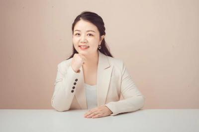 Nancy Huang sits behind a desk smiling with her chin resting on her hand. She has long black hair.