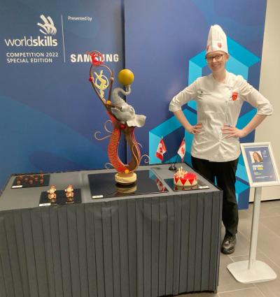 Emma Kilgannon wears her chef’s uniform as she stands beside a table with the various desserts and items she created.