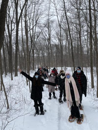 A group of people wearing snowshoes walk through a snow-covered forest.