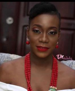 Olatoke Awoseyi smiles softly at the camera in a closeup, wearing a red necklace and off-the shoulder white top.