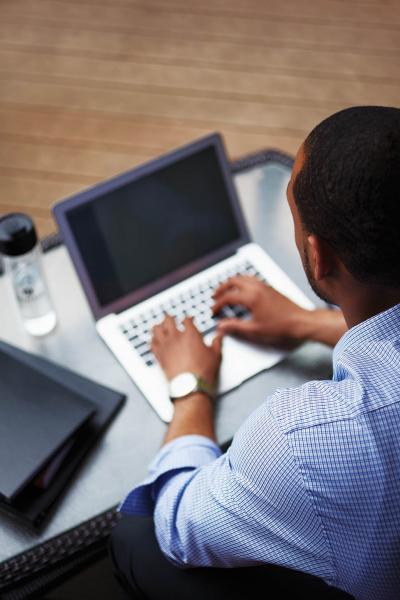 A person is seen from behind, sitting at a computer. The screen is visible over their shoulder and they are typing.