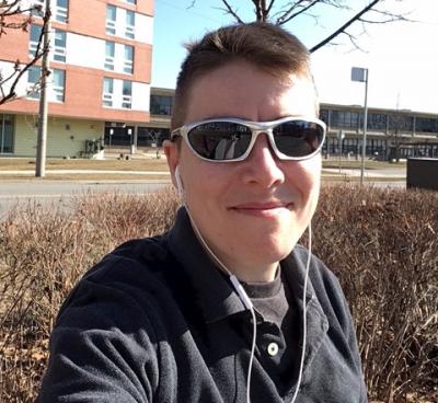 D Merkley takes a selfie across the street from a residence building at Humber's Lakeshore campus, wearing sunglasses