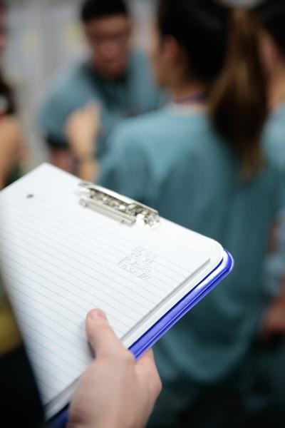 a professor takes notes as paramedic students practice skills