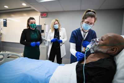 A Humber Nursing student tends to a mannequin in a hospital bed as two local MPs look on