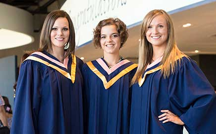 three graduates pose in their blue gowns