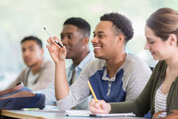 young man raising hand in class with other people in the row around him